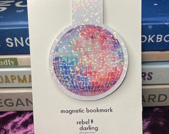 Puede incluir: Un marcapáginas magnético con forma de bola de discoteca plateada con purpurina y el texto "rebel darling gifts & party favors" en una tarjeta blanca.