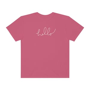 Op de afbeelding: Een roze T-shirt met het woord "hello" in wit cursief op de voorkant.