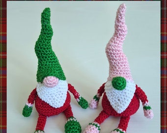 Pode incluir: Dois gnomos de crochê sentados lado a lado. O gnomo à esquerda tem um chapéu verde e o gnomo à direita tem um chapéu rosa. Ambos os gnomos têm corpos vermelhos, barbas brancas e detalhes verdes e rosa.