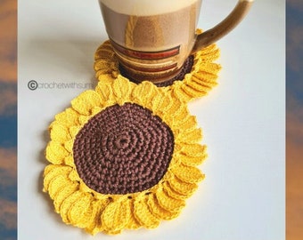 May include: Two crocheted sunflower coasters in yellow and brown. The coasters are on a white surface with a mug on top of one of the coasters.