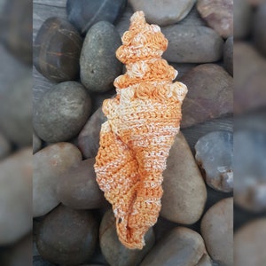 Może przedstawiać: Ręcznie robiona muszelka w odcieniach pomarańczowego i białego. Muszelka jest wykonana ściegiem fakturowanym i ma spiralny kształt.