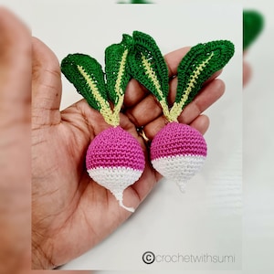 May include: Two crocheted radishes with green leaves, pink tops, and white bottoms.