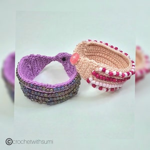 Può includere: Due braccialetti all'uncinetto, uno viola con perline iridescenti e uno pesca con perline rosa e bianche.