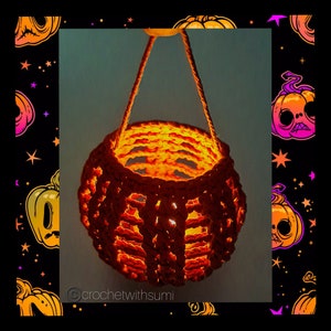 Könnte beinhalten: Eine gehäkelte orangefarbene Laterne mit warmem, leuchtendem Inneren. Die Laterne ist rund mit einem offenen Webmuster und wird von einer passenden orangefarbenen Kordel gehalten. Der Hintergrund zeigt ein Halloween-Motiv mit Kürbissen und Sternen.
