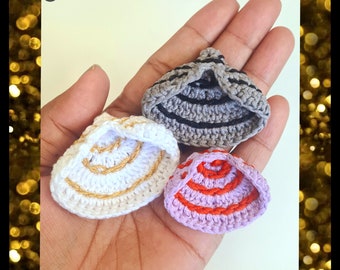 Puede incluir: Tres sombreros de ganchillo en diferentes colores y patrones. Los sombreros son grises con rayas negras, blancos con ribetes dorados y morados con rayas rojas.
