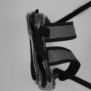 May include: A clear plastic bag with a gray and black strap. The bag has a zipper closure and is designed to be worn on the shoulder.