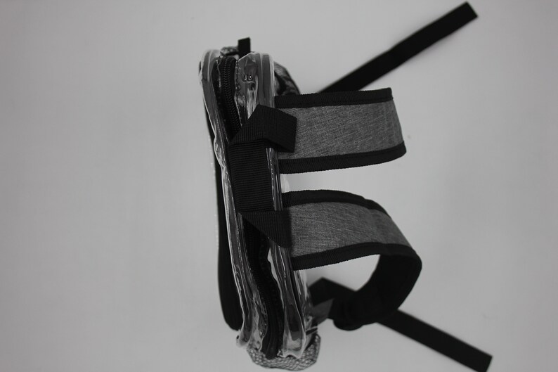 May include: A clear plastic bag with a gray and black strap. The bag has a zipper closure and is designed to be worn on the shoulder.