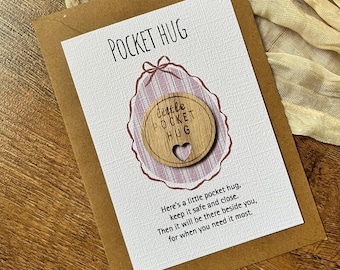 May include: A Pocket Hug card with a wooden heart-shaped charm. The card is brown with the words "POCKET HUG" at the top. The charm has the words "little POCKET HUG" and a heart cutout. The card includes a message.