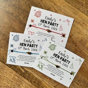 Może przedstawiać: Trzy białe karty z tekstem i ilustracjami na wieczór panieński. Każda karta ma dołączony sznurek w innym kolorze. Tekst brzmi "Emily's HEN PARTY 21st March 2026" z ilustracjami kuli dyskotekowej.