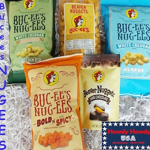 May include: A variety pack of Buc-ee's snacks, including white cheddar habanero, white cheddar, bold and spicy, and dark chocolate beaver nuggets. The bags are all blue and green with the Buc-ee's logo and mascot.