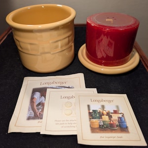 May include: A yellow ceramic basket-weave style container and a red candle on a matching saucer. The candle has a decorative design. Three Longaberger product information cards are also present.