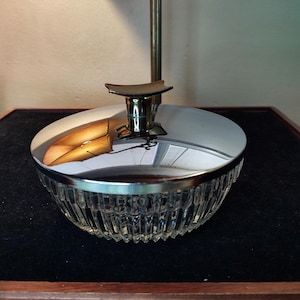 May include: A clear glass jar with a silver lid and a silver knob on top. The jar has a ribbed design and is sitting on a black surface.