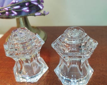 May include: A pair of clear glass salt and pepper shakers with a geometric design. The shakers have a hexagonal base and a square top.