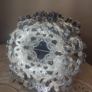 May include: A silver-plated, decorative, round, openwork napkin holder with a floral design.