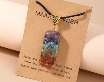 May include: A gold necklace with a rectangular pendant filled with colorful stones. The pendant has a wire design and the necklace is on a brown card with the text "MAKE WISH" and instructions to make a wish when the charm is worn through.