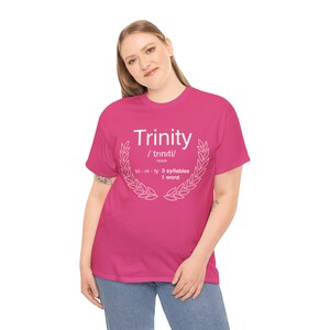 Può includere: Maglietta rosa con testo bianco che dice "Trinity /'triniti/ nome tri-ni-ty 3 sillabe 1 parola" con una corona di alloro bianca attorno al testo.