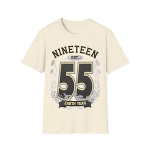 May include: A beige t-shirt with a black and gold graphic that says "NINETEEN EST. 55 EARTH YEAR".