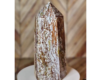 May include: A brown and white agate crystal point with a pointed top and a flat base. The crystal has a unique pattern of white and brown swirls and streaks.