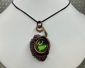 May include: A copper wire wrapped pendant necklace with a green glass cabochon. The necklace is on a black cord.