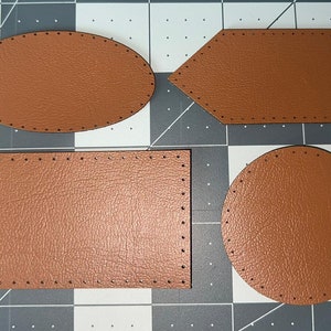 Puede incluir: Cuatro parches de cuero marrón con bordes cosidos. Los parches son de diferentes formas: ovalada, rectangular, hexagonal y circular.