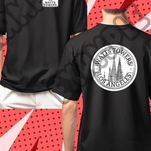 May include: Black t-shirts with white graphics. One shirt features a small rectangular logo that says "Watts Towers". The other shirt has a circular logo on the back with the words "Watts Towers Los Angeles" surrounding an illustration of the towers.