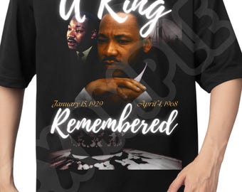 May include: Black t-shirt featuring a portrait of Martin Luther King Jr. with the words "A King Remembered" in white script. The dates "January 15, 1929" and "April 4, 1968" are also displayed.