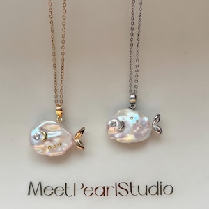 May include: Two fish-shaped pearl necklaces. One has a gold chain and accents, the other a silver chain. Each pendant features a large, iridescent pearl body, a small fin, and a gemstone eye. The text "Meet PearlStudio" is at the bottom.