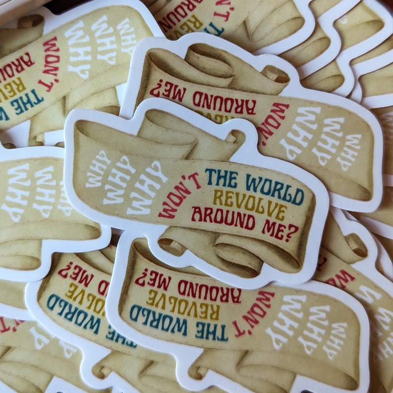 May include: A collection of stickers featuring a scroll design with the text "Why won't the world revolve around me?" in various colors. The stickers have a vintage, parchment-like appearance.