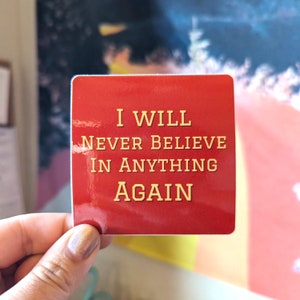 May include: Red square sticker with the text "I WILL NEVER BELIEVE IN ANYTHING AGAIN" in gold letters.
