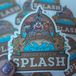 May include: A sticker featuring a cartoon scene with a rabbit, bear, and fox on a log flume ride. The sticker has the words "Briar Patch" and "Splash" in a brown font. The background is light blue and brown.