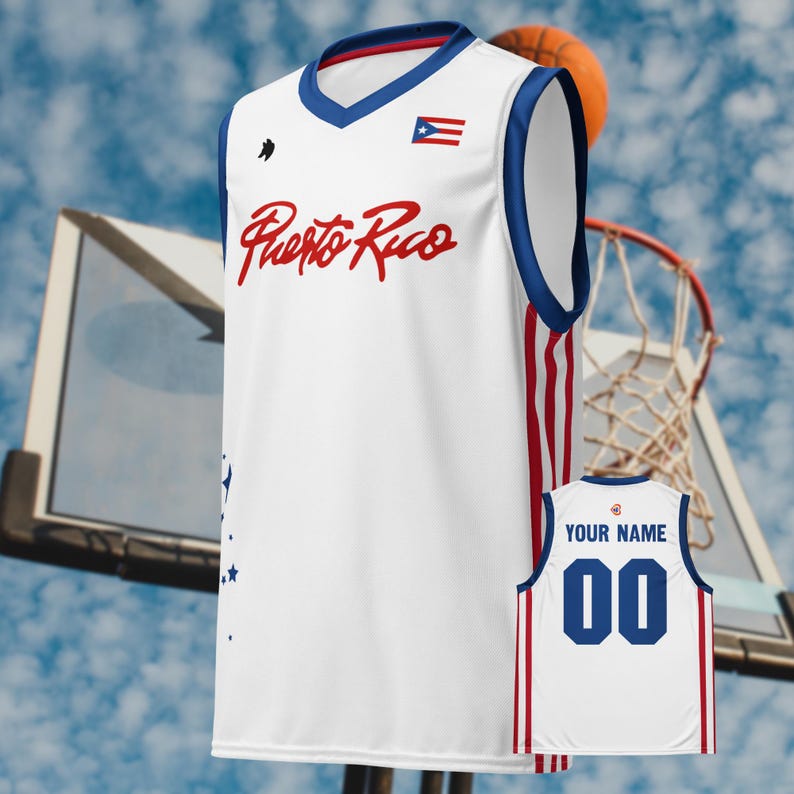 May include: White basketball jersey with blue and red accents. Features the text "Puerto Rico" in red script, a small flag, and a customizable back with "YOUR NAME" and the number "00". A basketball hoop and ball are in the background.