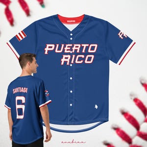 Puede incluir: Una camiseta de béisbol azul con ribetes blancos y rojos. La camiseta tiene "PUERTO RICO" escrito en rojo y blanco en la parte delantera. La parte posterior de la camiseta tiene el número "6" y el nombre "SANTIAGO" en blanco.