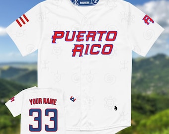 Puede incluir: Camiseta de béisbol blanca con "PUERTO RICO" en letras rojas y azules. La camiseta tiene un cuello azul con diseños blancos y la marca "ANUBIXX". Una camiseta más pequeña muestra "YOUR NAME" y el número "33" en rojo y azul.