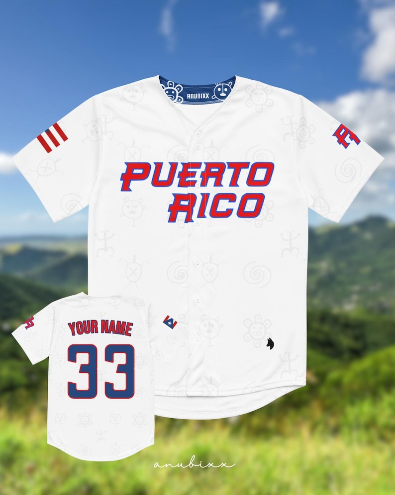 Puede incluir: Camiseta de b&eacute;isbol blanca con "PUERTO RICO" en letras rojas y azules. La camiseta tiene un cuello azul con dise&ntilde;os blancos y la marca "ANUBIXX". Una camiseta m&aacute;s peque&ntilde;a muestra "YOUR NAME" y el n&uacute;mero "33" en rojo y azul.