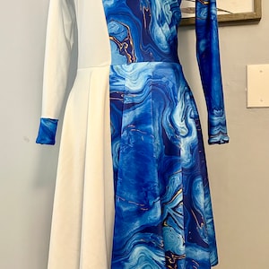 May include: A white and blue dress with a high neck and long sleeves. The dress has a blue marble pattern on one side and a white fabric on the other side. The dress is on a mannequin.