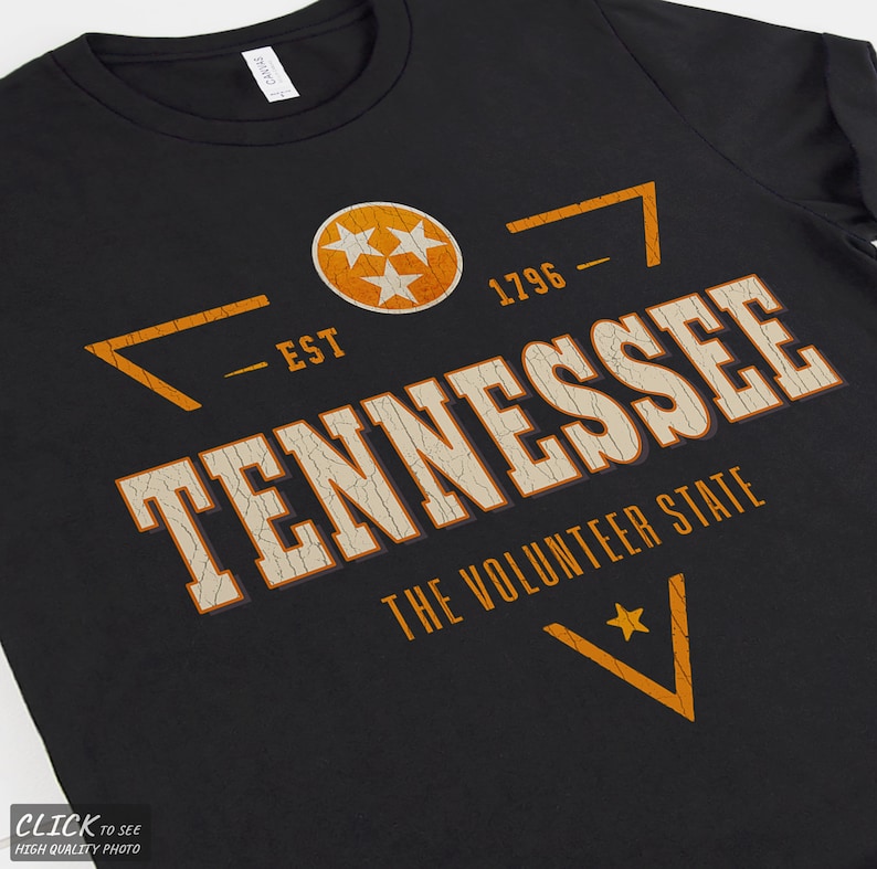 May include: A black t-shirt featuring a distressed orange and white graphic that reads TENNESSEE THE VOLUNTEER STATE, EST 1796, and includes a circular emblem with three stars, all printed in a weathered, cracked texture style.