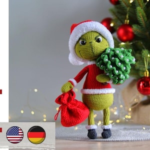 Puede incluir: Un personaje verde tejido a ganchillo con un gorro de Papá Noel y un traje rojo, sosteniendo un pequeño árbol de Navidad y un saco rojo. El personaje está frente a un árbol de Navidad con adornos rojos. La imagen también incluye el texto "pdf pattern".