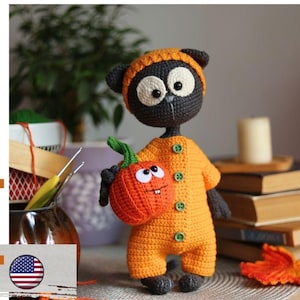 May include: A black crocheted cat doll wearing an orange hat and an orange onesie with four green buttons. The cat holds a small orange crocheted pumpkin with white eyes and a stitched mouth. The text "pdf pattern" is visible on the left side.