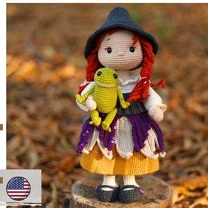 May include: A crochet doll with red hair wearing a black pointed hat, a white blouse, a dark gray vest, and a yellow skirt, holding a small green frog. The text 'pdf pattern' is visible on the left side along with a small American flag icon.