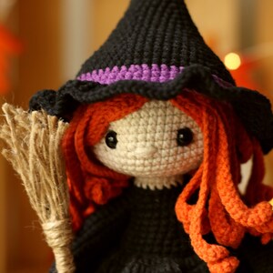 Peut inclure: Une poup&eacute;e de sorci&egrave;re en crochet avec un chapeau noir, des cheveux orange et un balai brun. La poup&eacute;e porte une robe noire et a un visage blanc avec des yeux noirs.