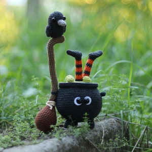 May include: A black crocheted cauldron with a witch's legs sticking out of the top. The cauldron has googly eyes and a brown crocheted broom.