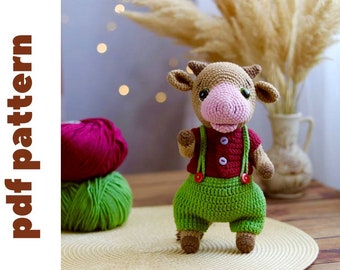 May include: A crocheted brown cow toy wearing a red and green outfit with red buttons. The toy is standing on a woven mat.
