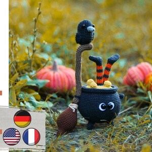 Puede incluir: Caldero de bruja de Halloween tejido a crochet con un cuervo negro posado en la parte superior, sosteniendo una escoba. El caldero tiene ojos saltones y está lleno de hilo naranja y negro. Las piernas de la bruja sobresalen del caldero, con medias rayadas naranja y negro.