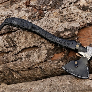 May include: A black leather axe with a raven head handle and intricate knotwork design. The axe head is silver with a detailed pattern.