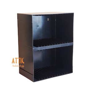 May include: Black two-tiered storage shelf with slatted dividers. The shelf is rectangular and has a simple, utilitarian design. The logo "ATTIC Archaeology" is visible in the lower left corner.