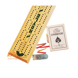 May include: A wooden cribbage board with the word "HOYLE" in green, along with a booklet titled "HOW TO ENJOY PLAYING CRIBBAGE." The set includes wooden pegs in red and natural wood colors, and a metal peg holder.