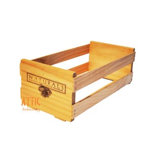 May include: A rectangular wooden crate with a light brown finish. The crate has a slatted design and features the word "NATURALS" in a rectangular label, along with a pine cone illustration. The words "NATURAL FINE STORAGE PRODUCTS" are also visible.