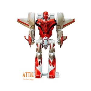 May include: A red, white, and silver Spider-Man Transformer toy. The toy has a Spider-Man head and chest, with jet wings and robot legs. The toy is standing upright. The text "ATTIC Archaeology" is at the bottom.