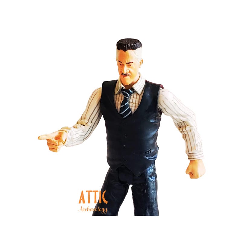 May include: A figurine of a man in a black vest, striped shirt, and tie, pointing with his right index finger. The figure has a mustache and a distinctive hairstyle. The text "ATTIC Archaeology" is visible at the bottom.