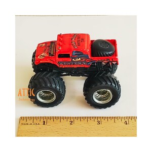 Pode incluir: Brinquedo de caminh&atilde;o monstro vermelho com "Wastern Rebellion" e "Renegade" impressos no lado. O caminh&atilde;o tem pneus grandes pretos e um pneu sobressalente na ca&ccedil;amba.